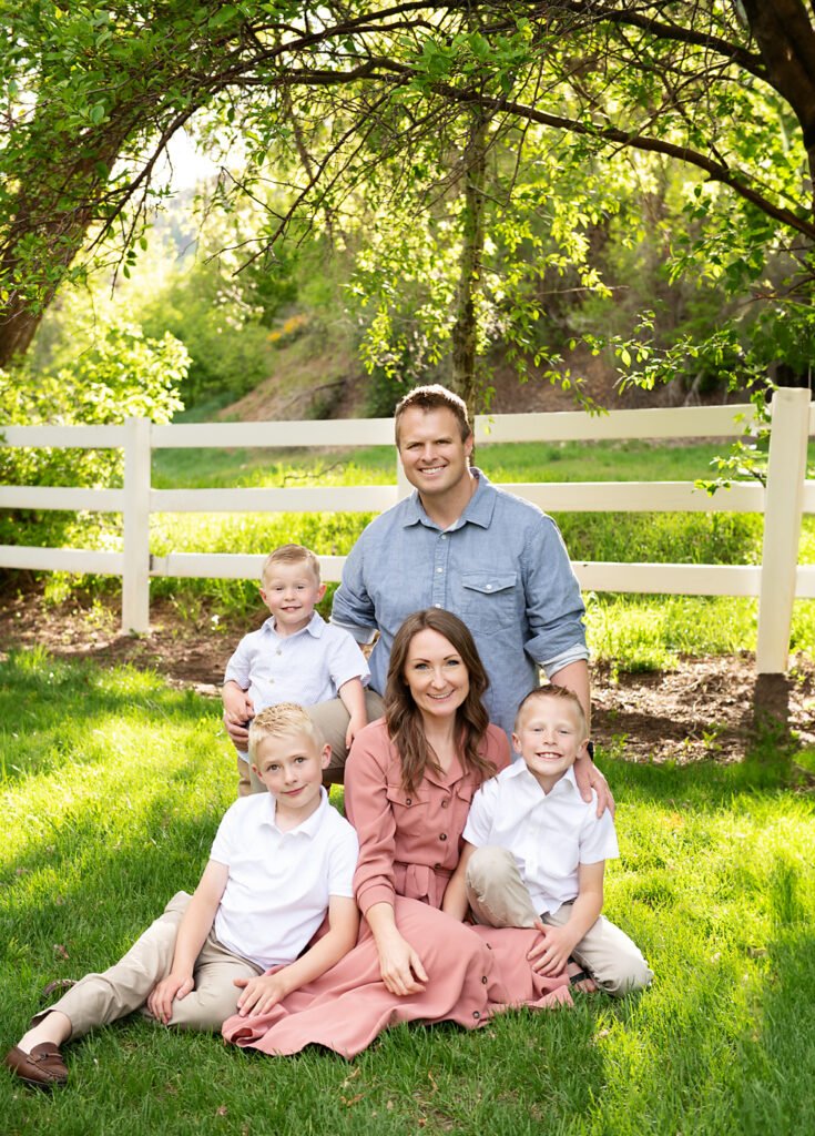 Utah Family Picture of family sitting on grass in front of fence and trees